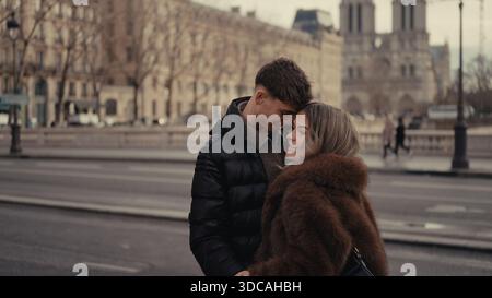 Ein romantisches Paar umarmt sich in Paris, Frankreich, mit der Kathedrale Notre Dame im Hintergrund. Das Paar trägt Wintermäntel, die Affec zeigen Stockfoto