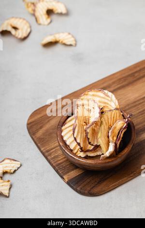 Apfelchips in einer Holzschale auf hellgrauem Hintergrund. Ein gesunder und köstlicher Snack voller Vitamine. Geeignet für Vegetarier. Stockfoto
