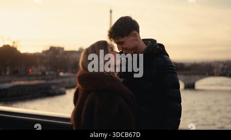 Ein romantisches Paar umarmt sich auf einer Brücke über die seine in Paris Frankreich mit dem Eiffelturm, der bei Sonnenuntergang im Hintergrund sichtbar ist. Dieses Bild ist s Stockfoto