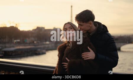 Ein romantisches Paar umarmt sich auf einer Brücke in Paris Frankreich mit dem Eiffelturm, der bei Sonnenuntergang im Hintergrund sichtbar ist Stockfoto