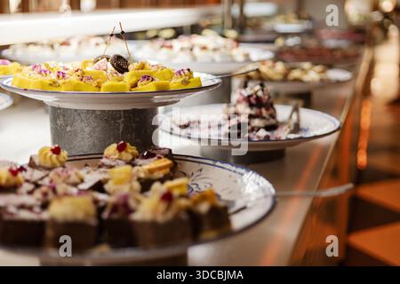 Die Teller sind mit verschiedenen Arten von Kuchen und Gebäck gefüllt, die auf einem Tisch angeordnet sind. Gäste können bei dieser Buffetveranstaltung in t Stockfoto