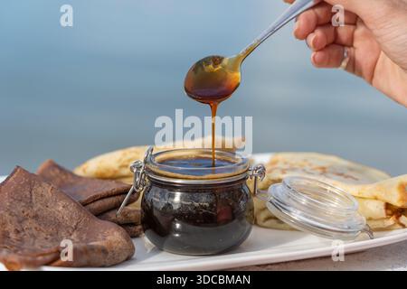 Frau, die Honig auf leckere Pfannkuchen auf den weißen Teller gießt, Nahaufnahme Stockfoto