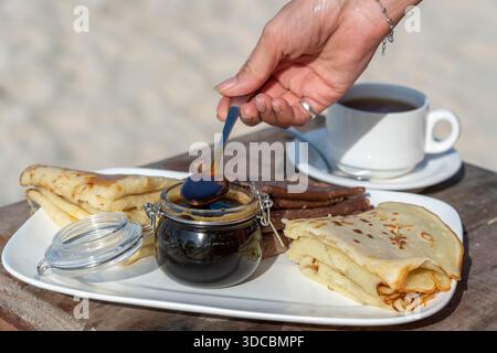 Frau, die Honig auf leckere Pfannkuchen auf den weißen Teller gießt, Nahaufnahme Stockfoto