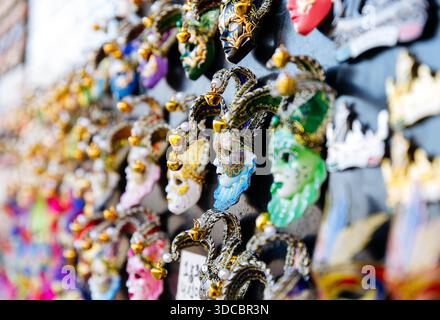 Farbenfrohe venezianische Karnevalsmasken mit Narrenmotiven an der Wand. Stockfoto