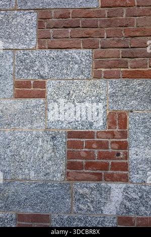 Eine strukturierte Wand aus roten Ziegelsteinen und grauen Granitblöcken schafft eine markante, urbane Kulisse mit starkem Kontrast und Tiefe, die sich für Architektur, Stockfoto