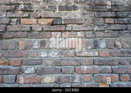 Eine verwitterte Ziegelwand mit alten roten und braunen Ziegeln, abgenutztem Mörtel und strukturierten Oberflächen. Idealer Hintergrund für Architektur, Geschichte oder rustikale Landschaft Stockfoto