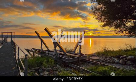 Blick auf den idyllischen Sonnenuntergang am Ufer des Sees. Im Vordergrund befindet sich eine Konstruktion für Yachten und ein Metallpier. Stockfoto