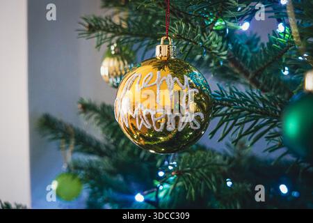 Goldene Weihnachtskugel mit froher Weihnachtsinschrift auf verziertem Baum Stockfoto