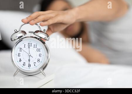 Mann, der morgens nach dem Wecker auf dem Nachttisch greift Stockfoto