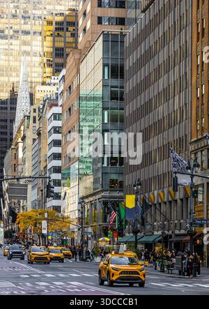 Überfüllte Fifth Avenue Szene mit mehreren gelben Taxis, hohen Gebäuden, Fahnen und Herbstbäumen in Midtown Manhattan; ideal für Reiseanzeigen und Geschäftsleute Stockfoto