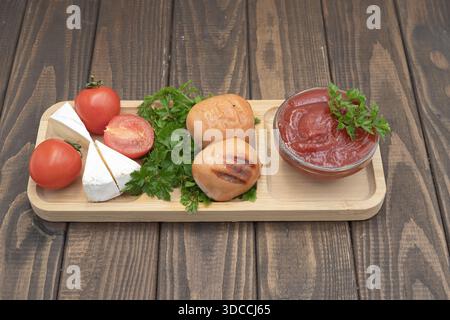 Gegrillte Würstchen mit Tomaten, Käse und Ketchup auf hölzernem Servierbrett, rustikale hausgemachte Speisen Stockfoto
