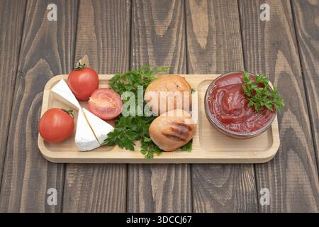 Gegrillte Würstchen mit Tomaten, Käse und Ketchup auf hölzernem Servierbrett, rustikale hausgemachte Speisen Stockfoto