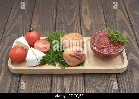 Gegrillte Würstchen mit Tomaten, Käse und Ketchup auf hölzernem Servierbrett, rustikale hausgemachte Speisen Stockfoto