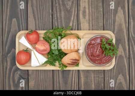 Gegrillte Würstchen mit Tomaten, Käse und Ketchup auf hölzernem Servierbrett, rustikale hausgemachte Speisen Stockfoto