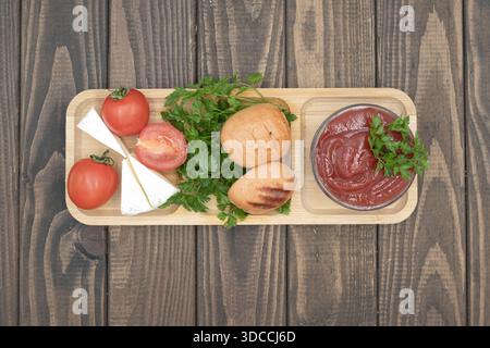 Gegrillte Würstchen mit Tomaten, Käse und Ketchup auf hölzernem Servierbrett, rustikale hausgemachte Speisen Stockfoto