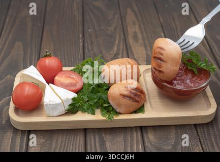 Gegrillte Würstchen mit Tomaten, Käse und Ketchup auf hölzernem Servierbrett, rustikale hausgemachte Speisen Stockfoto