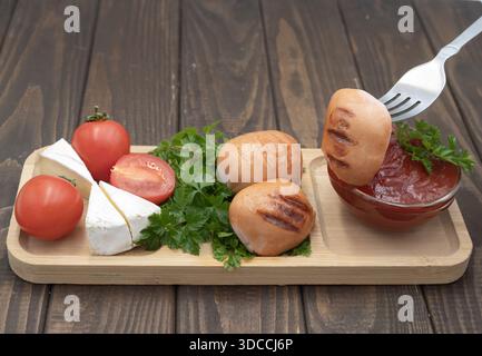 Gegrillte Würstchen mit Tomaten, Käse und Ketchup auf hölzernem Servierbrett, rustikale hausgemachte Speisen Stockfoto