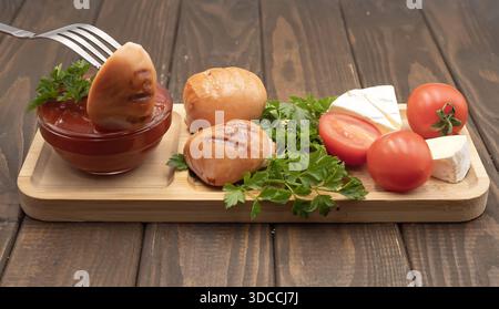 Gegrillte Würstchen mit Tomaten, Käse und Ketchup auf hölzernem Servierbrett, rustikale hausgemachte Speisen Stockfoto