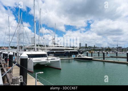 Eine Sammlung von Luxusyachten und Motorbooten, die im geschäftigen Viaduct Harbour mit der modernen Skyline von Auckland im Hintergrund vor Anker liegen. Stockfoto