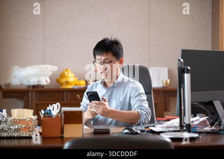 asiatischer Geschäftsmann mit Smartphone im Büro Stockfoto