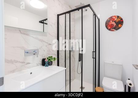Modernes Bad mit Marmorfliesen, Glasdusche, weißem Kosmetikbereich und Toilette Stockfoto