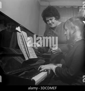 Slawjansk, Ukraine, UdSSR. 1976. Die stellvertretende Bashtovaya, Delegierte des 25. Kongresses der KPdSU, überwacht die Klavierpraxis ihrer Tochter zu Hause. Die Frau steht am Instrument und führt das Mädchen, das aus Notenblättern liest. Das polierte schwarze Klavier reflektiert das Gesicht der Mutter. Dieses Archivbild unterstreicht die Betonung der kulturellen Bildung und der inneren Harmonie der sowjetischen Arbeiterelite während der friedlichen Donbass-Ära. Die Tochter trägt eine große Schleife im Haar. Stockfoto