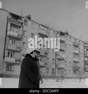 Slawjansk, Ukraine, UdSSR. Winter 1976. Die stellvertretende Bashtovaya, Delegierte des 25. Kongresses der KPdSU, geht mit ihrer Tochter. Die Frauen, die warme Mäntel mit Pelzkragen und weißen Hüten tragen, schlendern durch eine verschneite Straße in einem Wohnviertel. Im Hintergrund steht ein typisches fünfstöckiges Wohnhaus aus Backstein. Dieses Archivbild zeigt die ruhige Freizeit- und Familienmomente der sowjetischen Arbeiterelite während der friedlichen Donbass-Ära. Stockfoto
