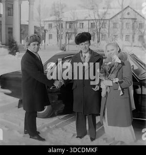 Slawjansk, Ukraine, UdSSR. Winter 1976. Deputy Rypalenko, Delegierter des 25. Kongresses der KPdSU, schüttelt einem Bräutigam während einer Hochzeit die Hand. Das Brautpaar steht neben einem prestigeträchtigen schwarzen Volga GAZ-24-Auto. Die Braut hält einen Strauß Calla-Lilien. Diese Outdoor-Szene in der Nähe des Kulturpalastes beleuchtet sowjetische Hochzeitstraditionen. Dieses Archivbild erfasst die sozialen Interaktionen und glücklichen Momente der arbeitenden Elite während der stabilen und friedlichen Donbass-Ära. Stockfoto