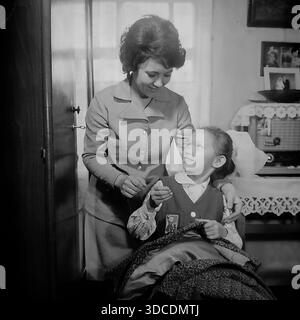 Slawjansk, Ukraine, UdSSR. Februar 1976. Delegierte des 25. Kongresses der KPdSU, Deputy Ladygina, eine Mitarbeiterin der Soda-Fabrik Slawiansk, verbringt Zeit mit ihrer Tochter zu Hause. Die Frau bringt dem Mädchen in Schuluniform und Octobrist-Sternenabzeichen bei, wie man nähen kann. Im Inneren befinden sich ein Vintage-Röhrenradio und Familienporträts an der Wand. Dieses Archivbild fängt das Leben der sowjetischen Arbeiterelite während der friedlichen Donbass-Ära ein. Stockfoto