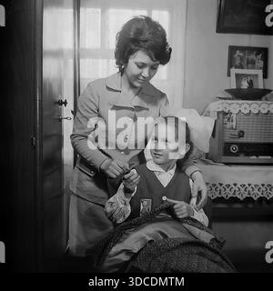 Slawjansk, Ukraine, UdSSR. Februar 1976. Delegierte des 25. Kongresses der KPdSU, Deputy Ladygina, eine Mitarbeiterin der Soda-Fabrik Slawiansk, verbringt Zeit mit ihrer Tochter zu Hause. Die Frau bringt dem Mädchen in Schuluniform und Octobrist-Sternenabzeichen bei, wie man nähen kann. Im Inneren befinden sich ein Vintage-Röhrenradio und Familienporträts an der Wand. Dieses Archivbild fängt das Leben der sowjetischen Arbeiterelite während der friedlichen Donbass-Ära ein. Stockfoto