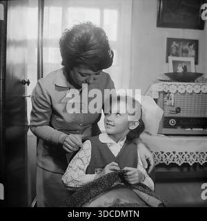 Slawjansk, Ukraine, UdSSR. Februar 1976. Delegierte des 25. Kongresses der KPdSU, Deputy Ladygina, eine Mitarbeiterin der Soda-Fabrik Slawiansk, verbringt Zeit mit ihrer Tochter zu Hause. Die Frau bringt dem Mädchen in Schuluniform und Octobrist-Sternenabzeichen bei, wie man nähen kann. Im Inneren befinden sich ein Vintage-Röhrenradio und Familienporträts an der Wand. Dieses Archivbild fängt das Leben der sowjetischen Arbeiterelite während der friedlichen Donbass-Ära ein. Stockfoto