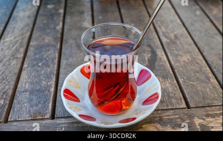 Nahaufnahme des traditionellen türkischen Tees (Cay), serviert in einem Tulpenglas mit einem Löffel auf einem Holztisch. Stockfoto