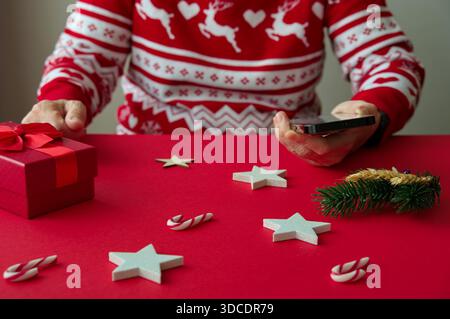 Mittelteil einer älteren Frau, die ein Handy mit Weihnachtsschmuck hält Stockfoto