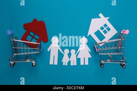 Papierfamilie zusammen und Einkaufswagen mit Haus auf blauem Hintergrund. Hauskauf-Konzept Stockfoto
