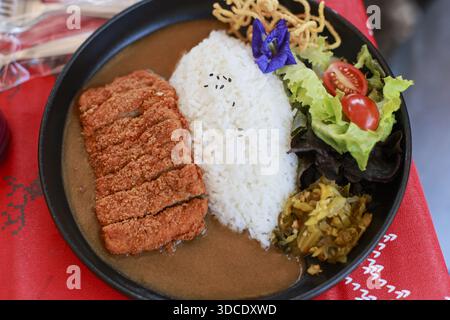 Blick von oben auf köstlichen japanischen Currypreis mit knusprigem Schweinekotelett und frischem Salatgemüse serviert auf schwarzem Teller zum Mittagessen, appetitlich und appetitlich Stockfoto