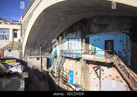 Schranktüren in einer Betonwand unter dem Bogen einer Brücke teilweise im Schatten mit Treppen, die zu ihnen führen, und Angelausrüstung daneben Stockfoto