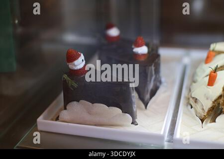 Köstliche Schokoladenkuchenscheibe mit niedlicher Erdbeerdekoration und leckerem Karottenkuchenstück auf weißem Tablett in Glasvitrine bei süßer Bäckerei Sho Stockfoto