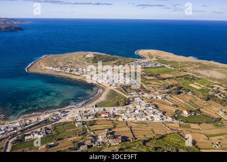 Aus der Vogelperspektive trifft das azurblaue Wasser auf die zerklüftete Küste, wo sich Gebäude inmitten von Feldern in Erdtönen schmiegen, Mellieha Bay, Malta. Stockfoto