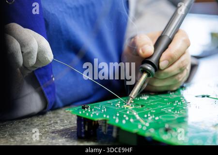 Nahaufnahme eines Technikers, der Lötkolben und Lötdraht verwendet, um Leiterplatten mit Flussrauch in der Elektronikwerkstatt zu überarbeiten Stockfoto