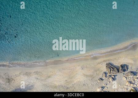 Aus der Vogelperspektive auf das türkisfarbene Meer, das sanft das Sandstrand küsst, gespickt mit Felsen, einer ruhigen Symphonie aus Blau und Beige, Paradise Bay, Mellieha, Malta Stockfoto