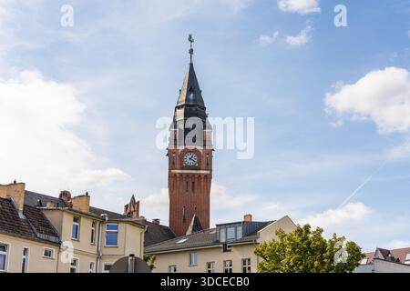 Blick auf das Rathaus Köpenick, der rote Backsteinturm, der einen blauen Himmel durchsticht, der von flauschigen Wolken gesäumt ist und sich von den malerischen Dächern abhebt Stockfoto
