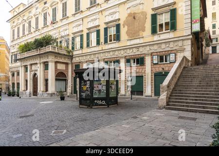 Genua, Italien - 25. Dezember 2022: Blick auf eine verwitterte Gebäudefassade mit grünen Fensterläden und Blick auf einen malerischen Platz mit Zeitungskiosk und Steinen Stockfoto