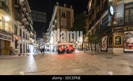 Madrid, Spanien - 09. November 2016: Blick auf die lebhafte Straßenszene bei Nacht, wo warmes Licht von einer Bar auf den kühlen Pflastersteinpflaster fließt, c Stockfoto