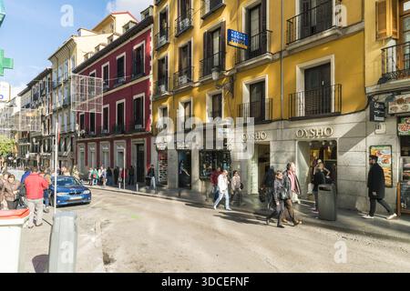 Madrid, Spanien - 09. November 2016: Blick auf die lebhafte Straße mit leuchtend gelben und roten Gebäuden, Fußgänger, die schlendern, und Geschäfte wie Oysho Lining Stockfoto