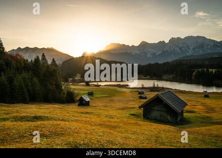 Blick auf goldene Gräser treffen auf den ruhigen See, der von majestätischen Bergen bewacht wird, während die Sonne durchbricht und den Himmel in warmen Tönen zeigt, Krun, G Stockfoto