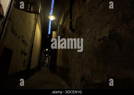 Sehr enge Gasse mit ein paar Graffiti und Straßenlaternen und einem offenen Geschäft weit in der Ferne in der Dämmerung Stockfoto