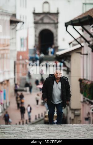 Quito, Ecuador - 17. Oktober 2025: Blick auf einen Mann steht entschlossen auf einer verwitterten Steintreppe, eingerahmt von den weichen Kolonialfassaden und dem dist Stockfoto