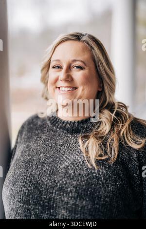 Blonde Frau lächelt im grauen Pullover-Porträt Stockfoto