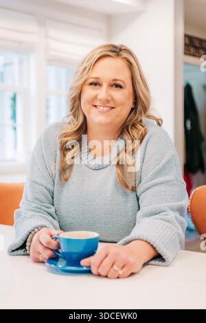 Frau lächelt und hält zu Hause eine Kaffeetasse Stockfoto