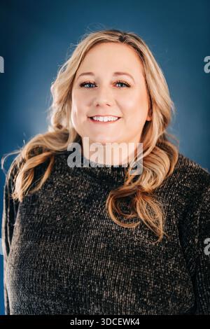 Lächelnde Frau in dunklem Pullover auf blauem Hintergrund Stockfoto